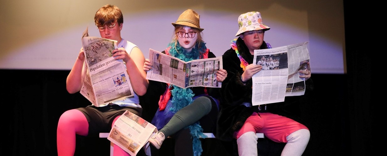 JHS production of History of Comedy Abridged, three clowns reading newspapers